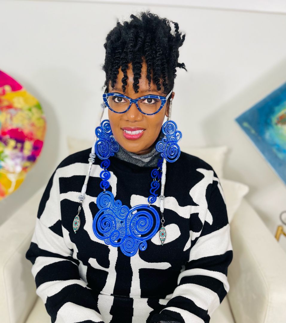 Photo of Ann-Marie Davy in black and white top wearing custom made blue and white earrings. She's also wearing blue and white glasses and she has natural hair with curly bangs